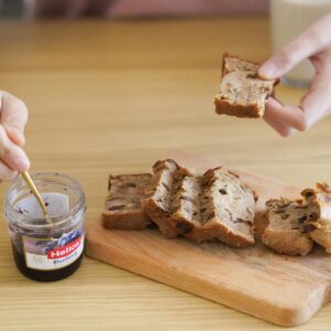 Hands spreading blueberry jam on slices of freshly baked bread on a wooden cutting board.