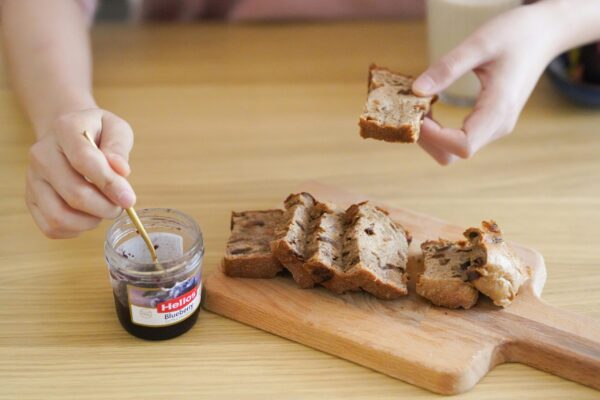 Hands spreading blueberry jam on slices of freshly baked bread on a wooden cutting board.