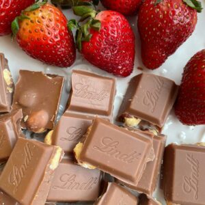 Close-up of Lindt chocolate pieces and fresh strawberries on a plate. Perfect for sweet lovers.